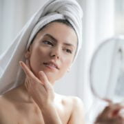 selective focus portrait photo of woman with a towel on head looking in the mirror
