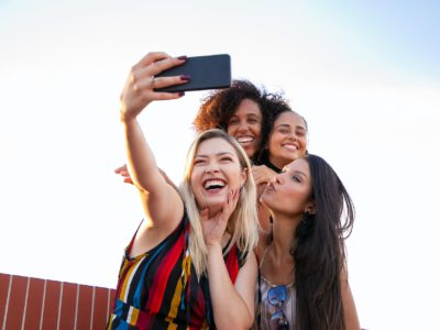 cheerful multiethnic girlfriends taking selfie on smartphone on sunny day