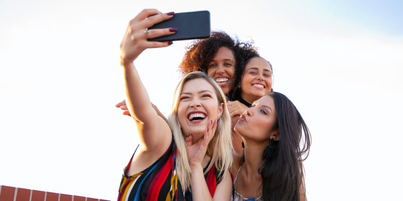 cheerful multiethnic girlfriends taking selfie on smartphone on sunny day