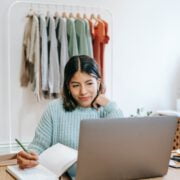 smiling woman browsing laptop while writing in planner