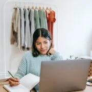smiling woman browsing laptop while writing in planner