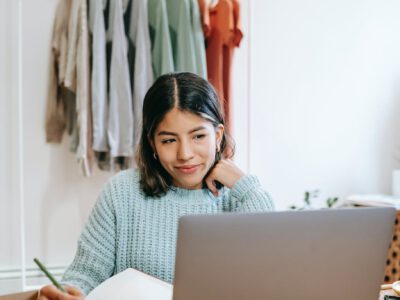 smiling woman browsing laptop while writing in planner