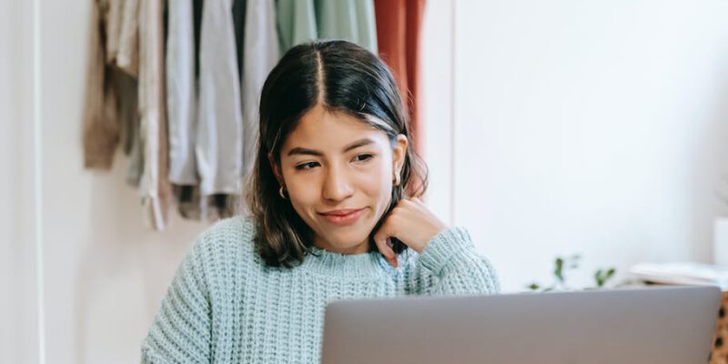 smiling woman browsing laptop while writing in planner